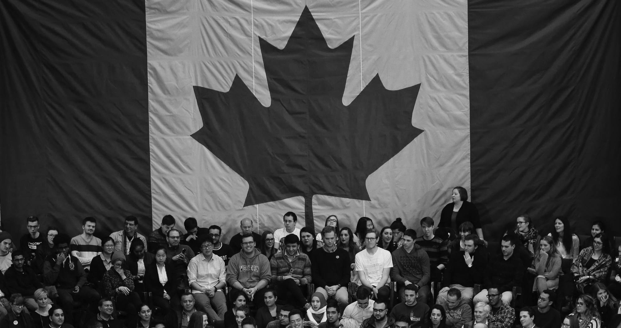 A large group of people sitting in front of a Canadian flag