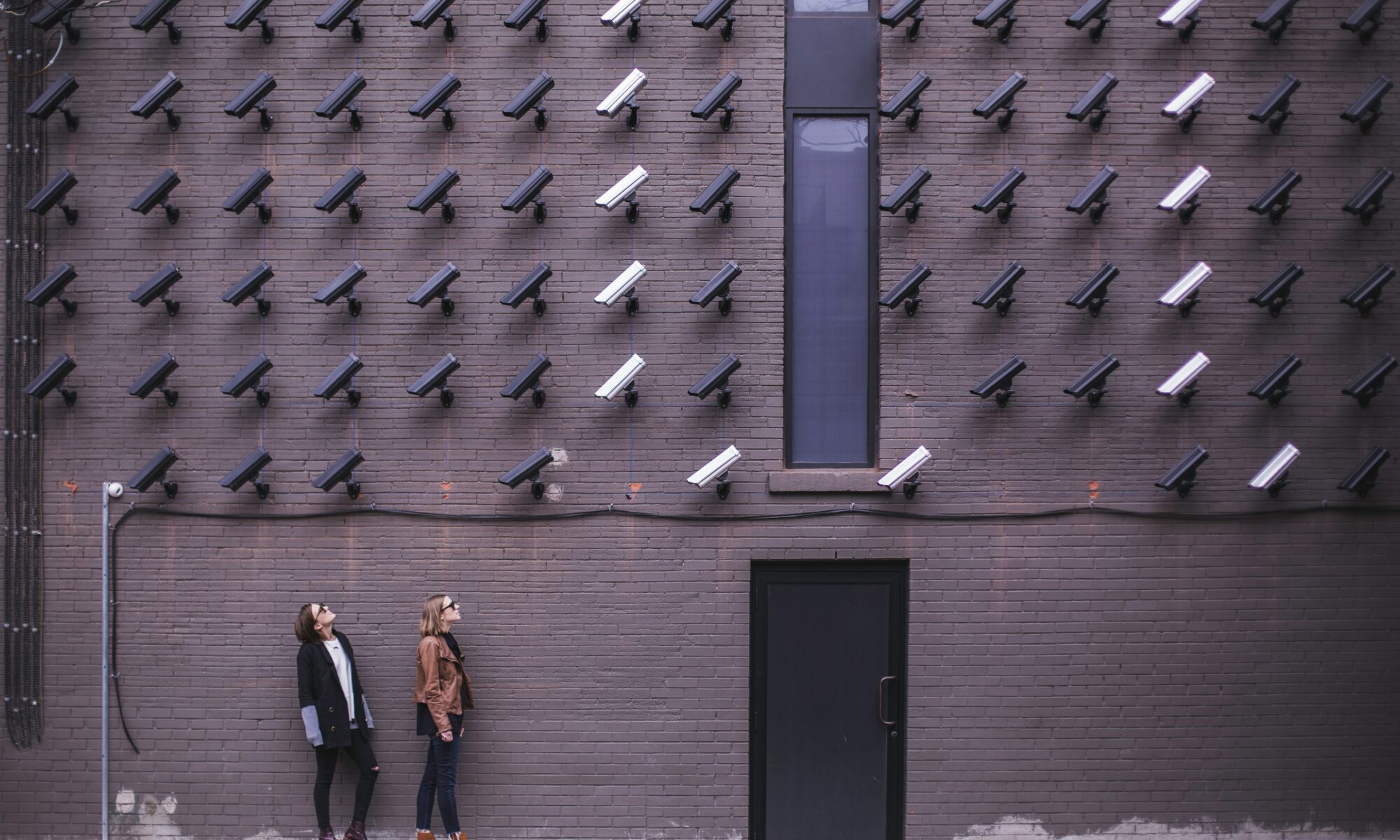 Two people looking up standing under a wall of CCTV cameras