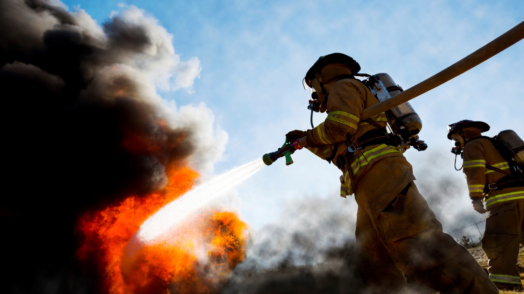 wo firefighters putting out a large fire with a hose