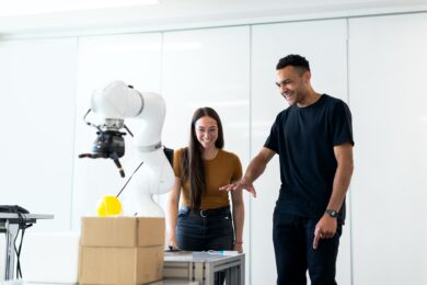 A man and woman looking at a robotic arm