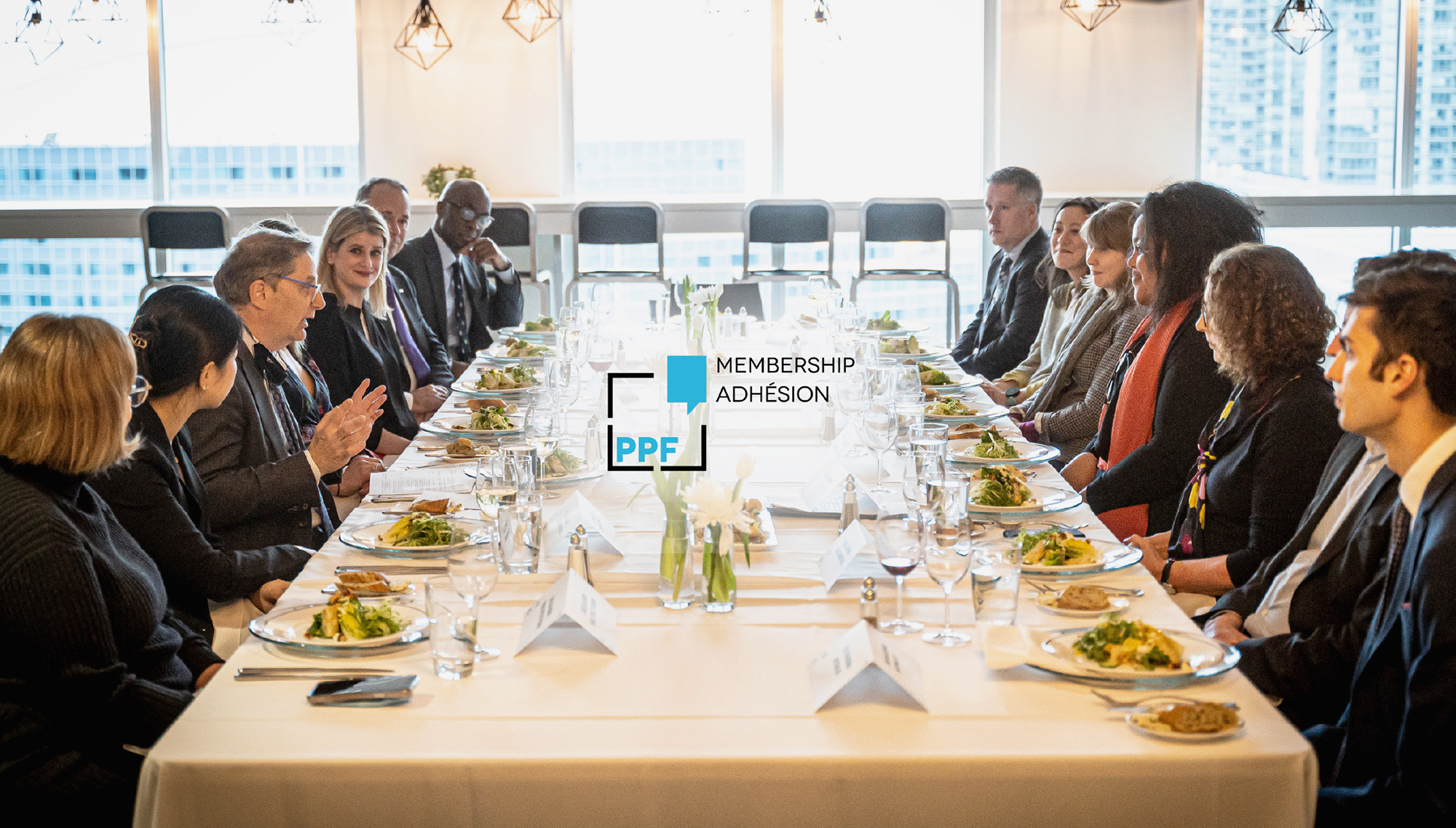 A group of people conversing at a table with the PPF Membership logo layered in the center