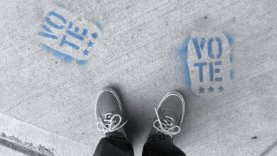 Top view of feet and the word 'VOTE' spray painted on the ground