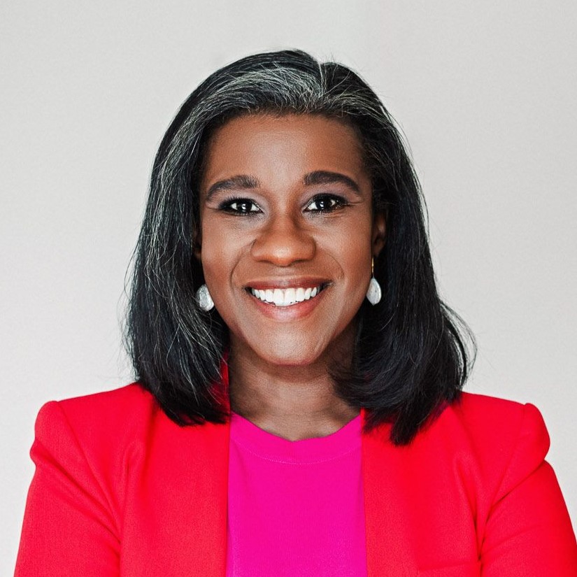 A person with medium length dark hair, wearing a red blazer and smiling